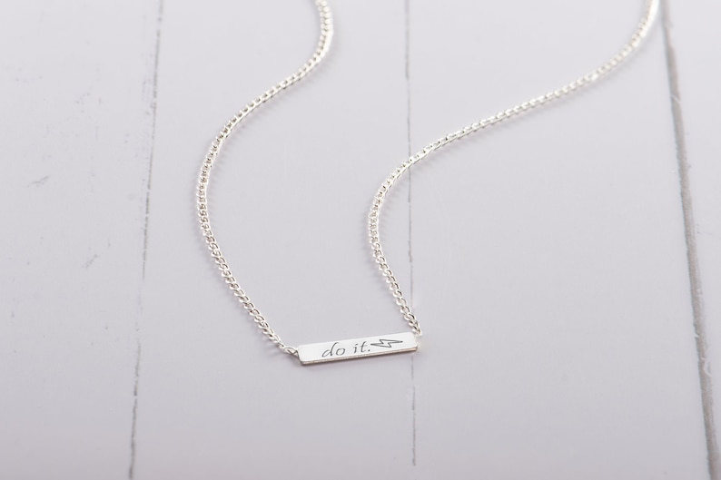 May include: A silver chain necklace with a small silver bar pendant that says "do it." with a lightning bolt symbol.
