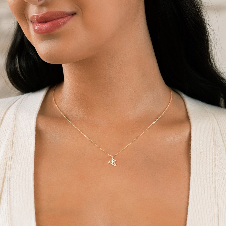 May include: A delicate gold chain necklace with a small, intricate pendant. The pendant is a stylized design of a flower.