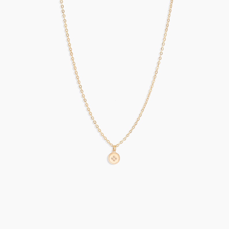 K&ouml;nnte beinhalten: Eine goldene Kettenkette mit einem kleinen runden Anh&auml;nger mit einem vierzackigen Stern.