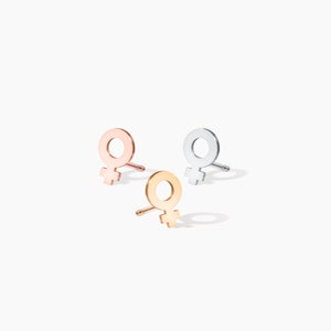 May include: Three pairs of earrings in silver, gold, and rose gold. Each earring features a simple female symbol design.
