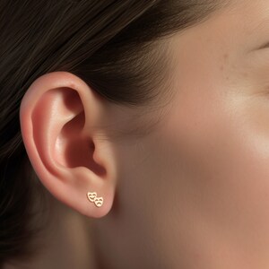 May include: A pair of gold-toned earrings featuring a small, stylized design of two theater masks, one smiling and one frowning.