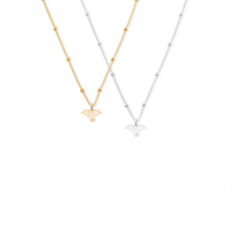 May include: Two delicate necklaces with a dragon pendant. One necklace is gold and the other is silver.