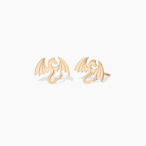May include: A pair of gold dragon stud earrings. The dragons are facing forward with their wings spread out.