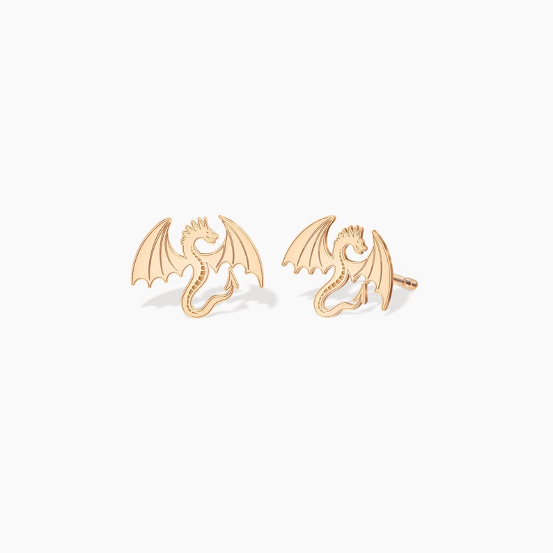 May include: A pair of gold dragon stud earrings. The dragons are facing forward with their wings spread out.