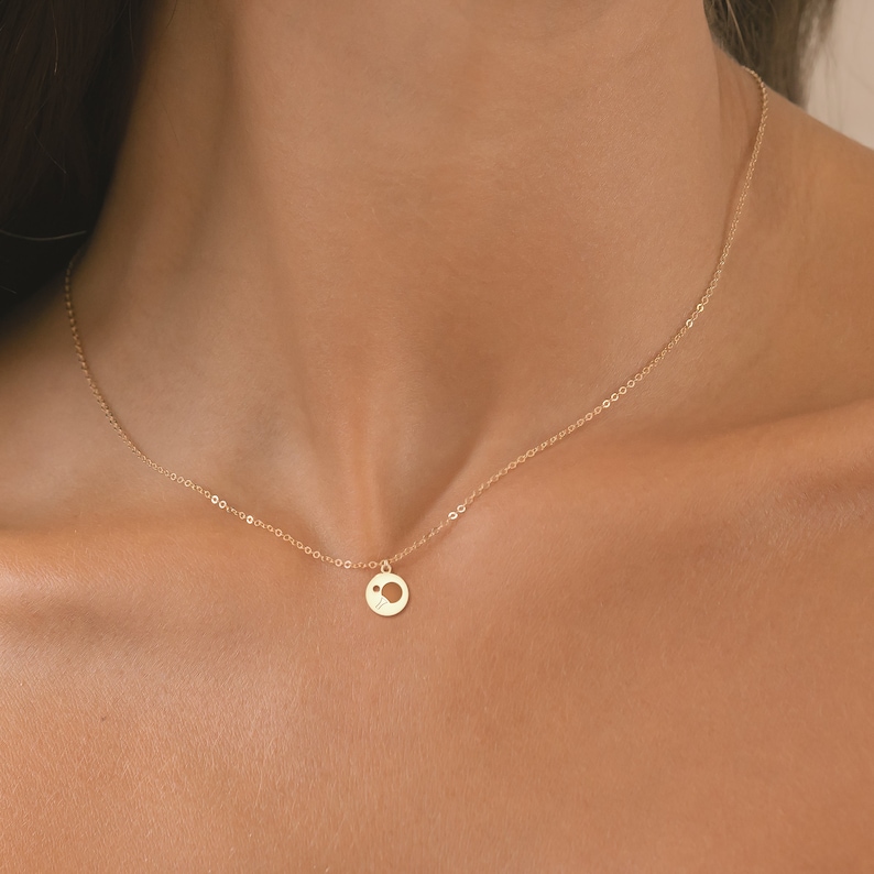 May include: A gold chain necklace with a small, round pendant featuring a cut-out circle design.