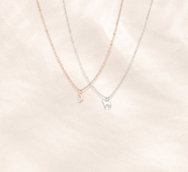 May include: Two delicate necklaces with silver chains. One necklace features a crescent moon pendant, while the other has a small wolf pendant.
