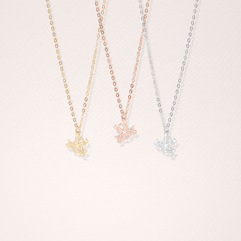 May include: Three delicate necklaces with geometric frog pendants. The necklaces are available in gold, rose gold, and silver.