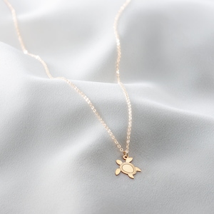 May include: A gold chain necklace with a small turtle pendant. The necklace is on a white fabric background.