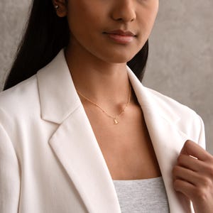 May include: A delicate gold necklace featuring a small pendant. The necklace is worn on a person, and the gold chain has small, evenly spaced beads. The pendant is a small, stylized shape.