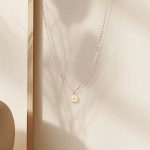 May include: A gold chain necklace with a small, round pendant featuring a compass design.