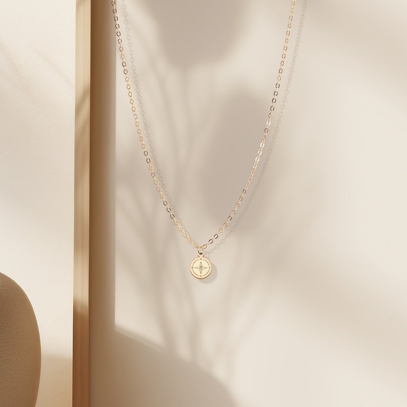May include: A gold chain necklace with a small, round pendant featuring a compass design.