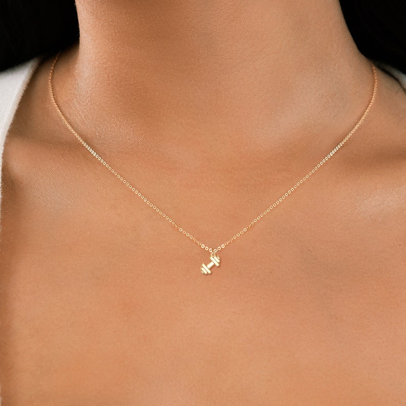 May include: A gold chain necklace with a small dumbbell pendant.