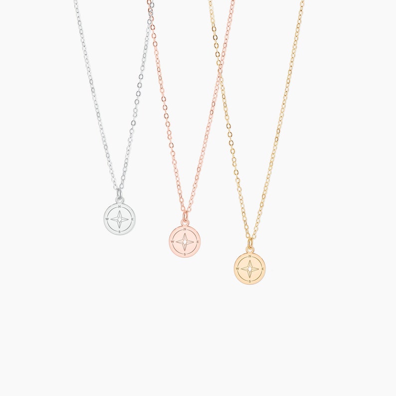 May include: Three delicate gold, silver, and rose gold necklaces with compass charms. Each charm features a compass rose with a four-pointed star in the center.