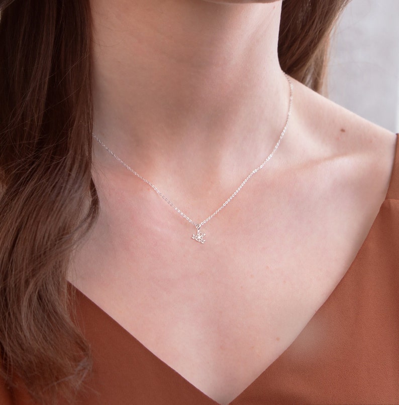 May include: A silver chain necklace with a delicate, floral pendant. The necklace is worn by a person with brown hair and a brown top.