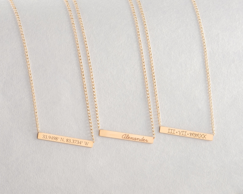 May include: Three gold necklaces with personalized bar pendants. The pendants are engraved with "33.9498&deg; N, 83.3734&deg; W", "Alexander", and "III&bull;VII&bull;MMXX".