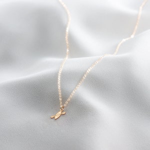 K&ouml;nnte beinhalten: Eine goldene Kettenkette mit einem kleinen goldenen Anh&auml;nger in Form eines Kanus. Die Kette liegt auf einem wei&szlig;en Stoffhintergrund.