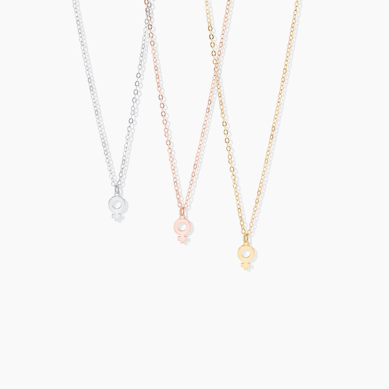 May include: Three delicate necklaces with a feminine symbol pendant. The necklaces are silver, rose gold, and gold.