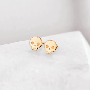 Puede incluir: Un par de pendientes de bot&oacute;n de calavera de oro. Los pendientes son peque&ntilde;os y delicados, y tienen un dise&ntilde;o simple y minimalista.