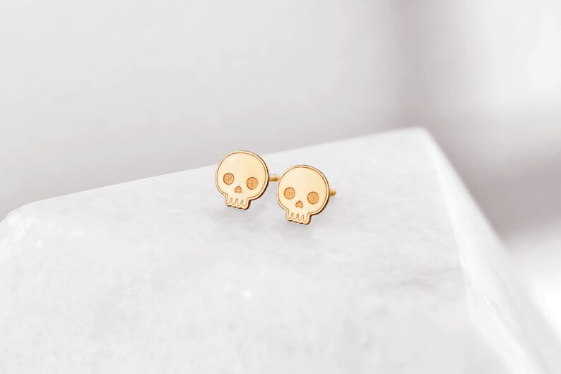 Puede incluir: Un par de pendientes de bot&oacute;n de calavera de oro. Los pendientes son peque&ntilde;os y delicados, y tienen un dise&ntilde;o simple y minimalista.