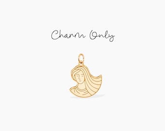 May include: Gold charm featuring a line drawing of a woman's face with long hair. The charm is shaped like a half-circle.