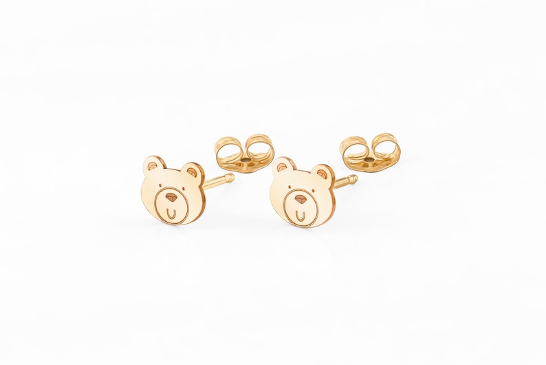 May include: A pair of gold bear stud earrings. The bear is outlined in a darker gold and has a smiling face.