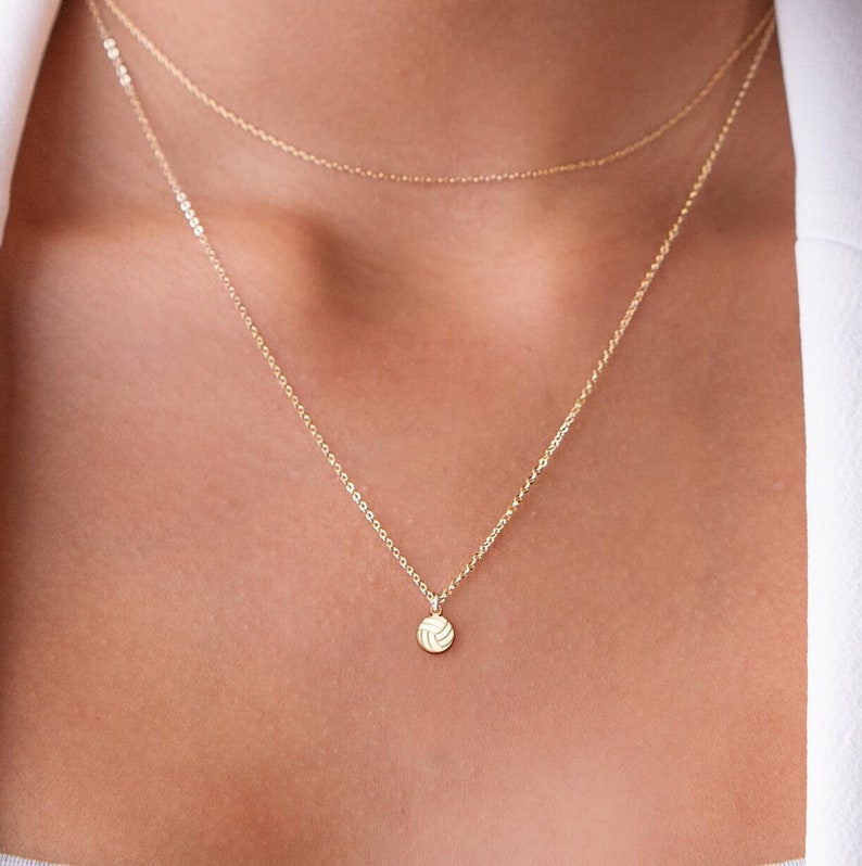 Pu&ograve; includere: Una collana con catena d'oro con un piccolo ciondolo a forma di pallavolo.