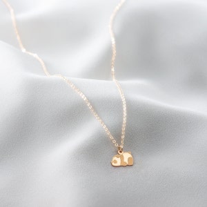 May include: A delicate gold-colored necklace with a small panda bear pendant. The panda is lying down, with a white and brown color scheme. The necklace chain is thin and hangs on a white, silky background.