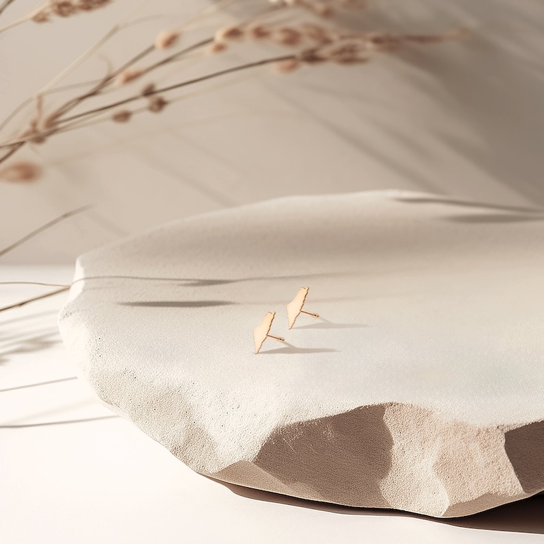 May include: A pair of gold-toned geometric earrings on a white textured surface.