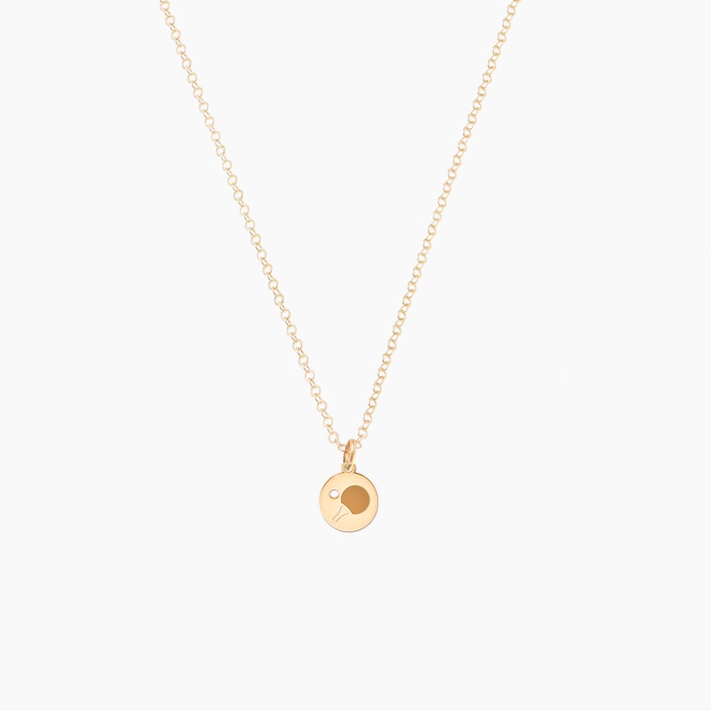 May include: A gold chain necklace with a small gold pendant featuring a table tennis bat and ball.