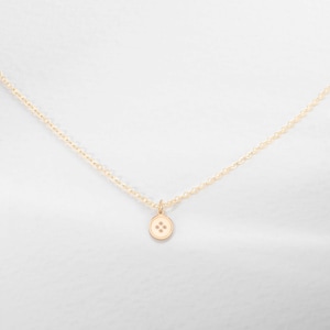 K&ouml;nnte beinhalten: Eine goldene Kettenkette mit einem kleinen goldenen Knopf-Anh&auml;nger. Der Knopf hat vier kleine Diamanten in der Mitte.