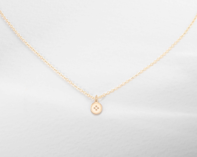 K&ouml;nnte beinhalten: Eine goldene Kettenkette mit einem kleinen goldenen Knopf-Anh&auml;nger. Der Knopf hat vier kleine Diamanten in der Mitte.