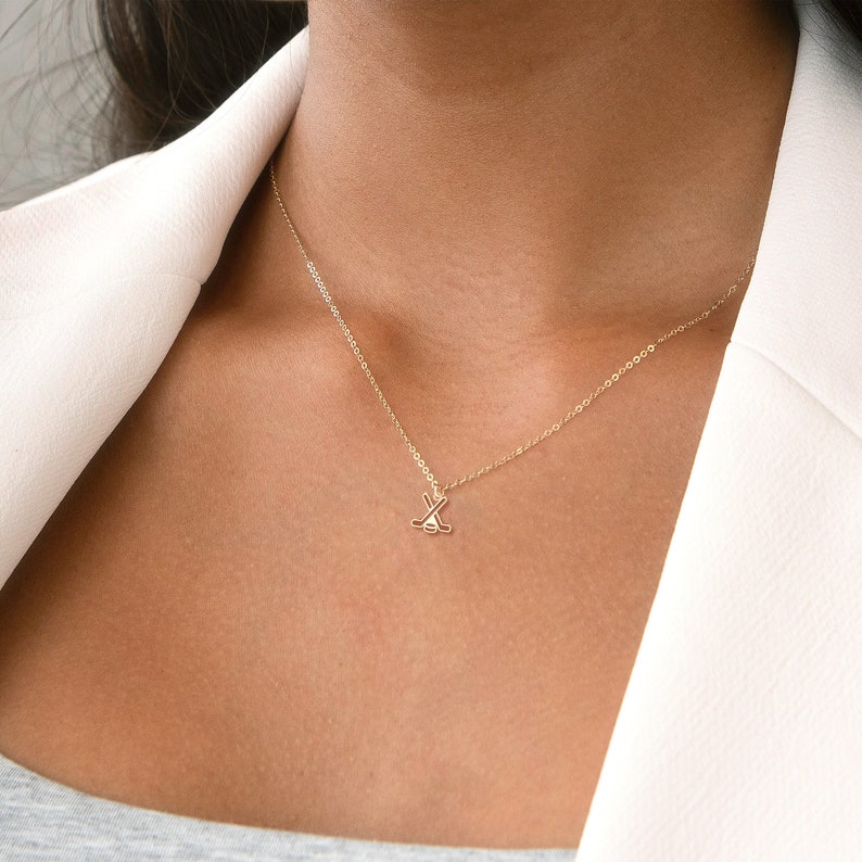 Pu&ograve; includere: Una collana d'oro con un piccolo ciondolo a forma di bastone da hockey.