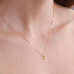 K&ouml;nnte beinhalten: Eine goldene Kettenkette mit einem kleinen, geometrischen Anh&auml;nger. Der Anh&auml;nger ist aus Gold gefertigt und hat ein schlichtes, modernes Design.