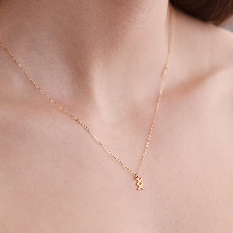 K&ouml;nnte beinhalten: Eine goldene Kettenkette mit einem kleinen, geometrischen Anh&auml;nger. Der Anh&auml;nger ist aus Gold gefertigt und hat ein schlichtes, modernes Design.
