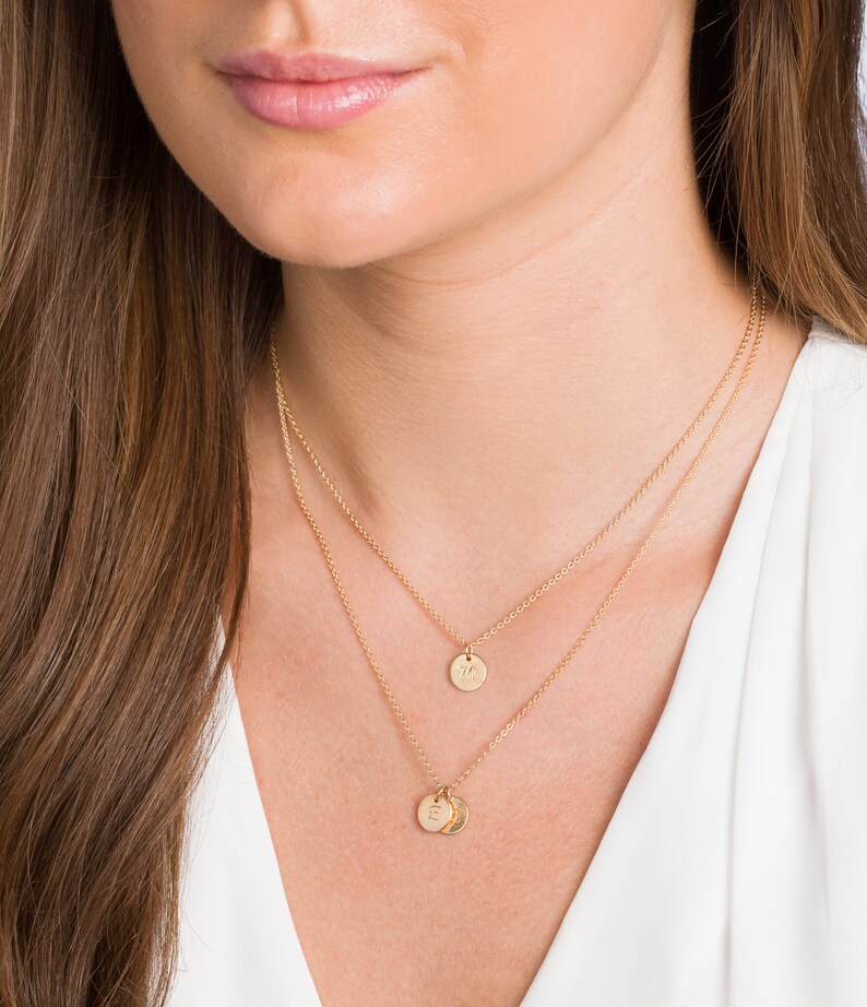 May include: A gold chain necklace with two small gold discs, one with the letter "M" and the other with the letter "S", hanging from it.