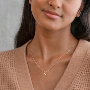May include: A gold chain necklace with a small double heart pendant. The necklace is worn by a person with brown skin.