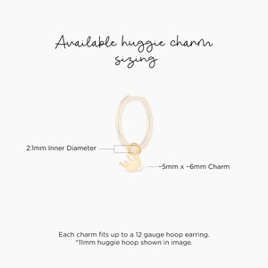 May include: Gold huggie hoop earring with a small crown charm. The hoop is 2.1 mm in diameter and the charm is approximately 5 mm by 6 mm. The charm fits up to a 12 gauge hoop earring.