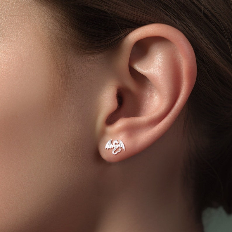May include: Silver dragon stud earrings. The earrings are small and delicate, and the dragon is facing to the right.