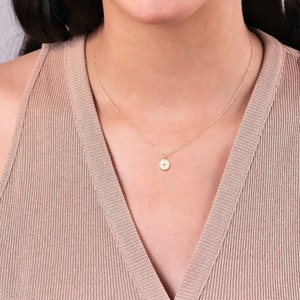 May include: A gold chain necklace with a small, round compass pendant. The pendant has a white background with a gold compass design.