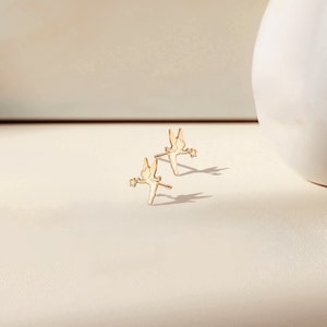 May include: A pair of gold-toned fairy stud earrings. Each earring features a delicate silhouette of a fairy with wings outstretched, holding a wand.