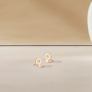 May include: A pair of gold-toned earrings with a female symbol design.