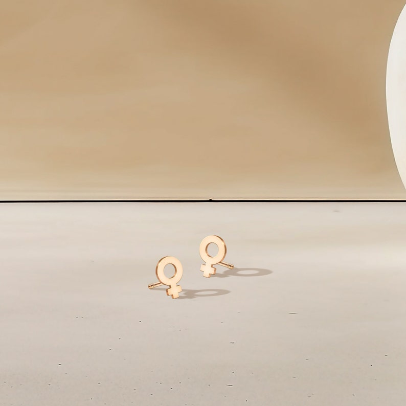May include: A pair of gold-toned earrings with a female symbol design.