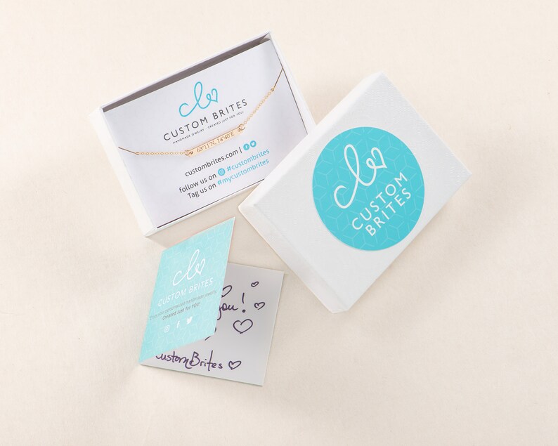 May include: A white box with a blue and white logo that says "clo CUSTOM BRITES". The box is open and a gold necklace with a charm that says "FINNE" is inside. There is a small card with the same logo and the text "custombrites.com | 00 follow us on @custombrites Tag us on #mycustombrites".