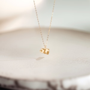 May include: A gold-colored necklace featuring a small panda bear pendant. The panda has brown and cream-colored accents. The chain is delicate and hangs from the pendant, creating a simple and elegant design.