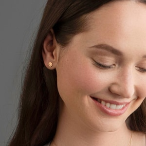 Puede incluir: Primer plano de la cara de una persona sonriendo con los ojos cerrados. Lleva peque&ntilde;os pendientes redondos de oro.
