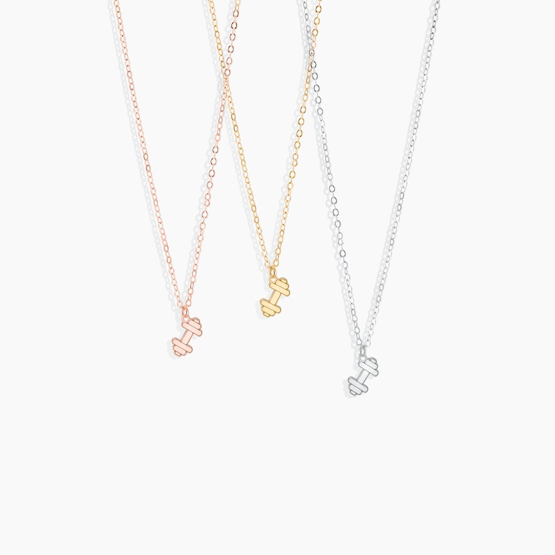 May include: Three delicate necklaces with dumbbell pendants. The necklaces are available in gold, rose gold, and silver.