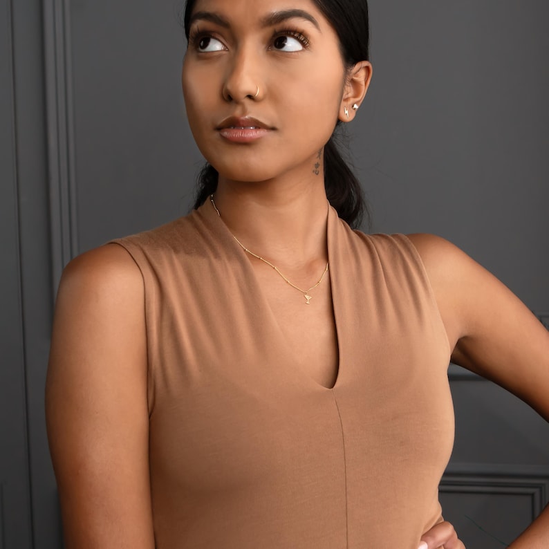 May include: A woman wearing a brown sleeveless top with a gold chain necklace and a small pendant.