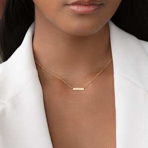 May include: A gold necklace with a delicate chain and a small bar pendant that says "dreamer".