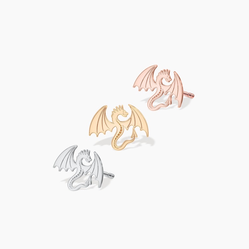 May include: Three dragon earrings in silver, gold, and rose gold. Each earring features a detailed dragon design with outstretched wings.
