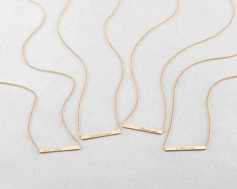 May include: Four gold necklaces with personalized bar pendants. The pendants are engraved with the text "4-27-2007", "Felix &hearts; Jasper", "Alexander", and "II. XXIII. XVII".